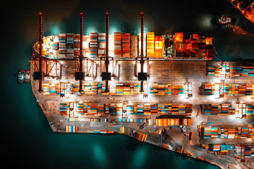 Drone photo of container terminal activities at night. Cainteinet ship is loaded with 4 cranes. 3 tugboats are on standby for assistance. Future Technologies In The Maritime Industry allow speed up cargo operations, reduce the number of errors and shorten port stays.