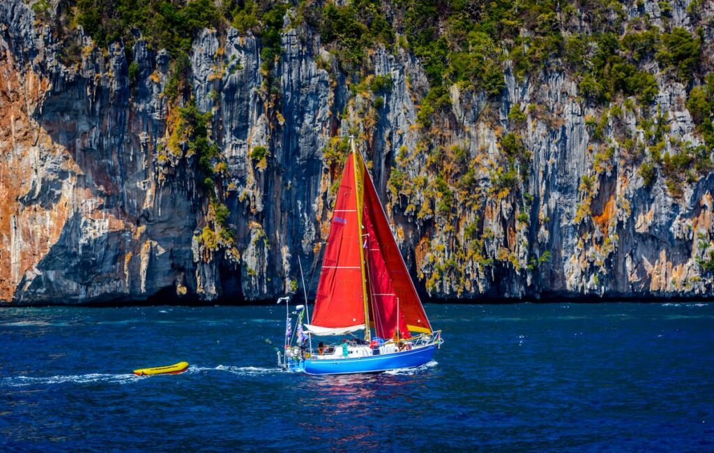 Brazilian sailboat with Tanbard sails undersway new rocky shore